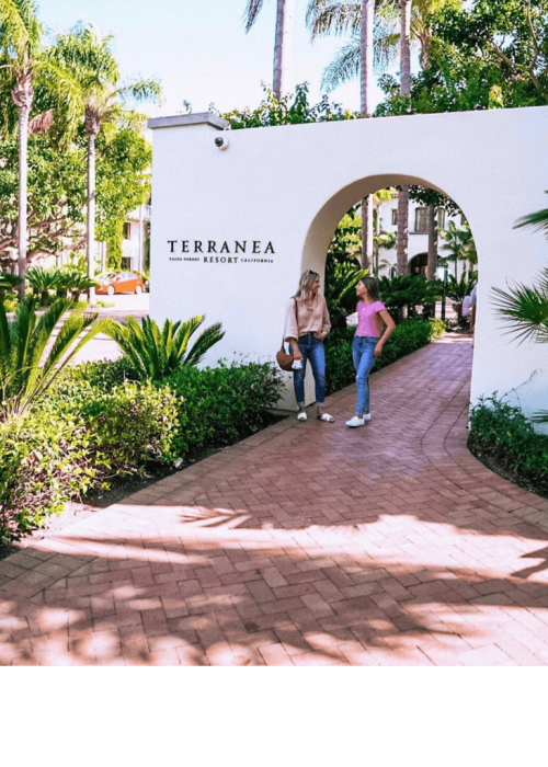 mom and daughter in front of hotel entrance with palm trees in background